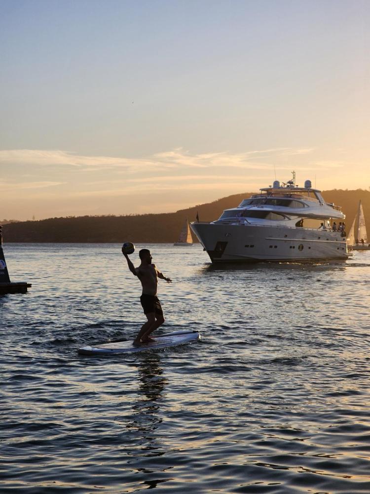 Person paddleboarding at sunset with a yacht in the background.