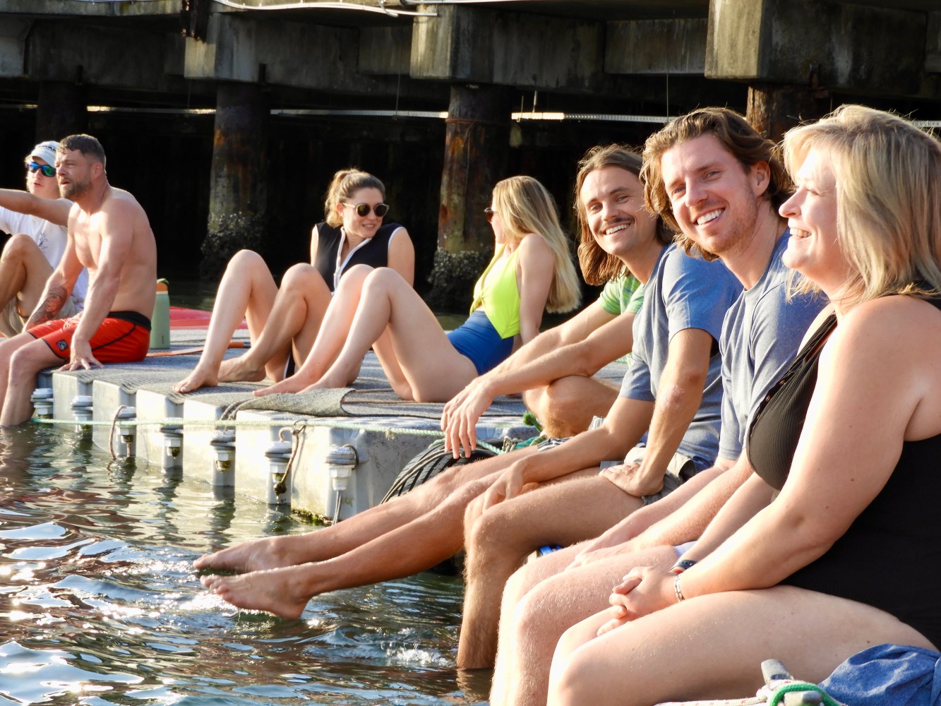 People sitting on a dock, laughing and dipping feet in water.